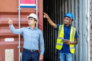 Hafenmanager und ein Kollege, der das Inventar verfolgt, während sie stehen, um die Ladecontainerbox vom Frachtfrachtschiff bei der Frachtcontainerschifffahrt auf einem großen kommerziellen Schifffahrtsdock zu positionieren foto