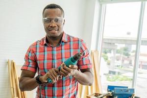 Arbeit in der Tischlerei. afroamerikaner glücklicher mann hält einen schraubendreher in der hand. Mensch in einer Holzbearbeitungswerkstatt. Baumeister am Arbeitsplatz. Zimmermann posiert am Arbeitsplatz. foto