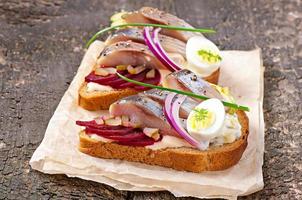 Sandwich aus Roggenbrot mit Hering, Rüben, Zwiebeln und Ei foto