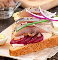 Sandwich aus Roggenbrot mit Hering, Rüben, Zwiebeln und Ei foto