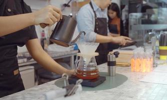 eine cafébetreiberin mit schürze gießt heißes wasser über gerösteten kaffeesatz, um kaffee für kunden im shop zuzubereiten.