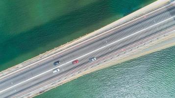 Luftaufnahme des Autofahrens auf einer Brücke mit natürlichen Waldbäumen, Sand, tropischem Strand und Wellen, die in die Küste rollen. foto