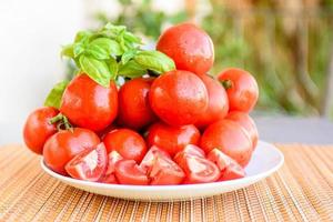 Zusammensetzung aus roten und runden Tomaten auf einem weißen Teller. mit einem Zweig Basilikum foto