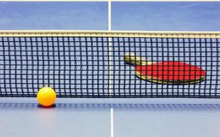 Tischtennisball, Schläger und Netz auf blauem Tisch