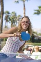junge Frau, die Tischtennis mit Leuten im Hintergrund spielt foto