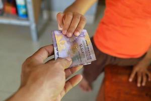 Die Hand eines Mannes gibt Rupiah-Banknoten an die Hand seines Sohnes foto