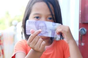 indonesisches kleines Mädchen, das ihren Mund mit Rupiah-Banknoten bedeckt foto