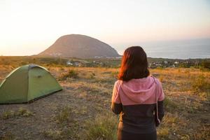 Frau begegnet der Morgendämmerung in den Bergen, freut sich über die Sonne. Panoramablick auf die Berge und das Meer von oben. Camping, Outdoor-Aktivitäten, Sportbergwandern, Familienreisen. ayu-dag, krim.