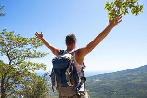 männlicher tourist mit einem rucksack auf einem berg mit erhobenen händen blickt auf das panorama der küste, der stadt, freut sich über die freiheit. Reisen, Trekking, Wandern, aktiver Lebensstil, Sporttourismus, Wandern. foto