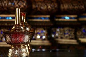 Goldenes Messing gießt zeremonielles Wasserglas und verwischt den einheimischen thailändischen Kunsthintergrund. Der Behälter, der im thailändischen Buddhismus verwendet wird, um Wasser der Widmung an Verstorbene zu gießen. Selektiver Fokus. foto