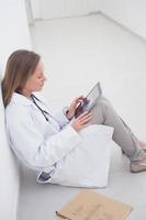 Arzt sitzt auf dem Boden und hält einen digitalen Tablet-PC foto
