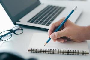 Geschäftsmann, der sich Notizen macht, fasst das Meeting online mit Laptop zusammen, arbeitet alleine und sitzt an Ihrem Schreibtisch. arbeiten von zu hause aus, nahaufnahme hände. foto