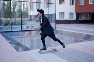 Konzept des jungen, schnellen und mobilen Managers. lustiger buisinessman auf skateboard im schwarzen anzug. foto
