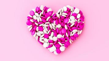 bunte Schoko-Knopf-Bonbons mit Schokolade überzogene Bohnen in Herzform auf rosa Hintergrund Valentinstag-Geburtstags-Hochzeits-Liebeskonzept