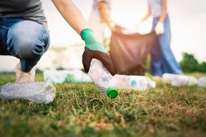 frauenhand, die müllplastikflasche zur reinigung im park aufhebt foto