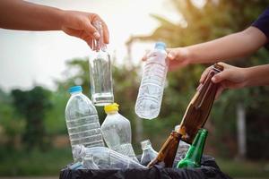 leute halten müllflasche plastik und glas in der hand und legen sie zur reinigung in den recyclingbeutel foto