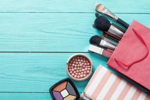 rahmen von make-up-produkten und zubehör mit roter tasche auf blauem holzhintergrund. Draufsicht und Attrappe.