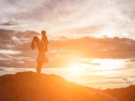 eine Silhouette eines glücklichen jungen Mädchens die Arme seiner liebenden Mutter für eine Umarmung vor dem Sonnenuntergang am Himmel an einem Sommertag. foto