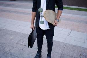 Konzept des jungen, schnellen und mobilen Managers. lustiger buisinessman auf skateboard im schwarzen anzug. foto