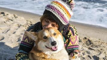 Junge glückliche Frau geht mit süßem Corgi-Hund am sonnigen Strand im Herbst spazieren foto