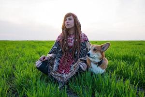 junge Frau im Poncho mit Corgi-Hund, der sich in den Frühlingsfeldern entspannt foto