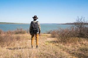 junger männlicher reisender mit hut nahe fluss foto