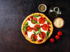 Heiße hausgemachte italienische Peperoni-Pizza mit Salami, Mozzarella auf einem dunkelbraunen Steintisch, Draufsicht, Kopierraum foto