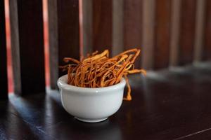 trockenes Cordyceps Militaris Myzel in weißer Schale mit Holzhintergrund. orange Heilpilz für eine gute Gesundheit. foto