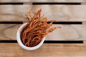 trockenes Cordyceps Militaris Myzel in weißer Schale mit Holzhintergrund. orange Heilpilz für eine gute Gesundheit. foto