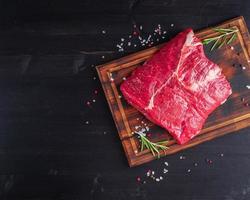 rohes Fleisch, Rindersteak mit Gewürzen auf Schneidebrett auf dunklem Hintergrund mit Rosmarin, foto