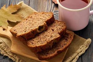 herbstessen - bananenbrotscheiben, eine tasse tee, trockene blätter, ein dunkler holztisch. Seitenansicht. foto