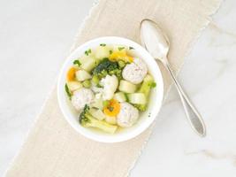 schüssel suppe, eine tasse brühe und gemüse, fleischbällchen aus puten und huhn, draufsicht foto