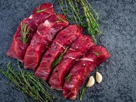 Rohes Fleisch, Rindersteak mit Gewürzen auf einem schwarzen Steintisch, Draufsicht foto