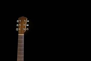 Der isolierte Kopf einer Akustikgitarre lehnte sich gegen den dunklen schwarzen Hintergrund. Platz kopieren. foto