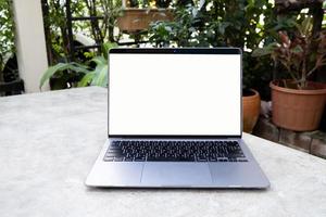 Laptop mit weißem leeren Bildschirm auf weißem Tisch. online-arbeit von zu hause aus und überall konzept. Gartenhaus Hintergrund. foto