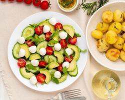 Frischer Salat mit Tomaten, Gurken, Rucola, Mozzarella und Avocado. Öl mit Gewürzen, Bratkartoffeln, Draufsicht, vertikal foto