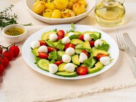Frischer Salat mit Tomaten, Gurken, Rucola, Mozzarella und Avocado. Öl mit Gewürzen, Bratkartoffeln, Seitenansicht hautnah foto