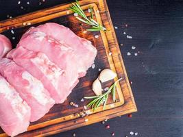Schweinesteak, rohes Karbonatfilet auf dunklem Hintergrund, Fleisch mit Rosmarin, Gewürze, Draufsicht foto