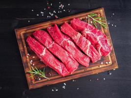 rohes Fleisch, Rindersteak mit Gewürzen auf Schneidebrett auf dunklem Hintergrund mit Rosmarin, foto