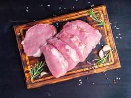 Schweinesteak, rohes Karbonatfilet auf dunklem Hintergrund, Fleisch mit Rosmarin, Gewürze, Draufsicht foto