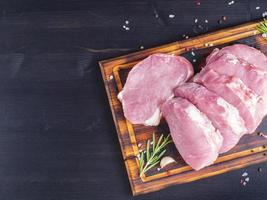 Schweinesteak, rohes Karbonatfilet auf dunklem Hintergrund, Fleisch mit Rosmarin, foto