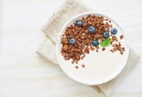 Joghurt mit Schokoladen-Granola, Heidelbeere. Frühstück auf einem weißen rustikalen Hintergrund, Draufsicht foto