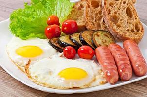 Englisches Frühstück - Spiegeleier, Würstchen, Auberginen und Tomaten foto