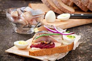 Sandwich aus Roggenbrot mit Hering, Rüben, Zwiebeln und Ei foto