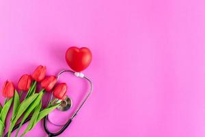 danke, ärzte und krankenschwestern. selektiver Fokus. glücklicher Tag der Krankenschwester. Tag der Gesundheit. Stethoskop, rote Tulpen, auf rosa Hintergrund. Gruß Hintergrund. Nationaler Tag des Arztes. Ansicht von oben, Platz rechts kopieren. foto