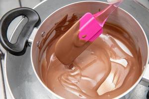 Kochtopf mit schmelzender Schokolade, der von Küchenchefs Hand auf dem Herd einer Küche entfernt wird, um süße Desserts zuzubereiten. Massenschokolade, die in einem Topf schmilzt. foto