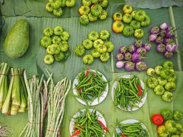 Haufen frischer grüner Auberginen, Chilis und Gemüse auf Bananenblättern zum Verkauf auf dem Markt. foto