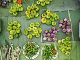 Haufen frischer grüner Auberginen, Chilis und Gemüse auf Bananenblättern zum Verkauf auf dem Markt. foto