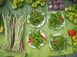 Haufen frischer grüner Auberginen, Chilis und Gemüse auf Bananenblättern zum Verkauf auf dem Markt. foto