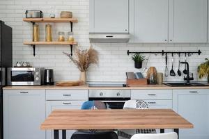 Inneneinrichtung der Küche im rustikalen Stil mit Vintage-Küchengeschirr und Holzwand. Weiße Möbel und Holzdekor in hellem Häuschen im Innenbereich. foto
